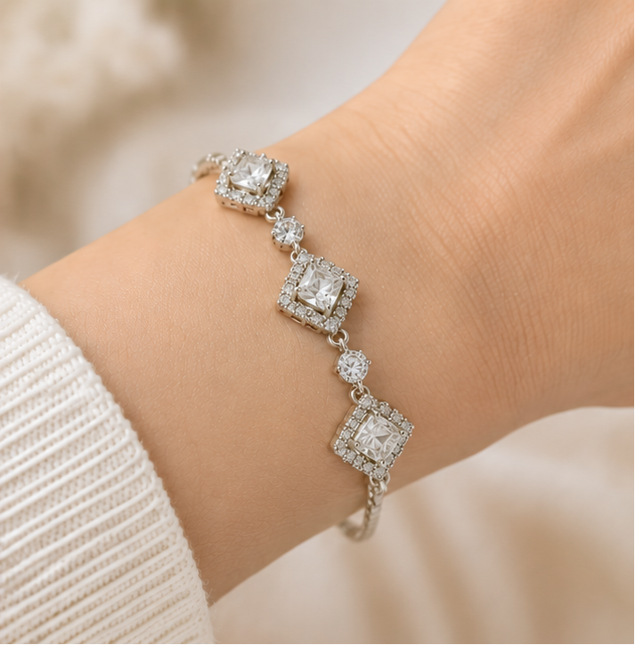 A silver-toned diamond chain bracelet shown in three views: a close-up of the dangling chain on the left, a mid-length view on a marble surface with flowers, and a worn view on a wrist.