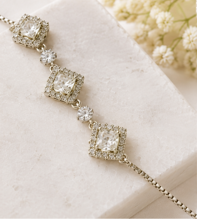A silver-toned diamond chain bracelet shown in three views: a close-up of the dangling chain on the left, a mid-length view on a marble surface with flowers, and a worn view on a wrist.