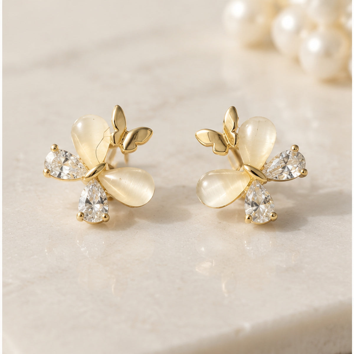 NZGO Pearl Cat's Eye butterfly stud earrings styled on neutral stone