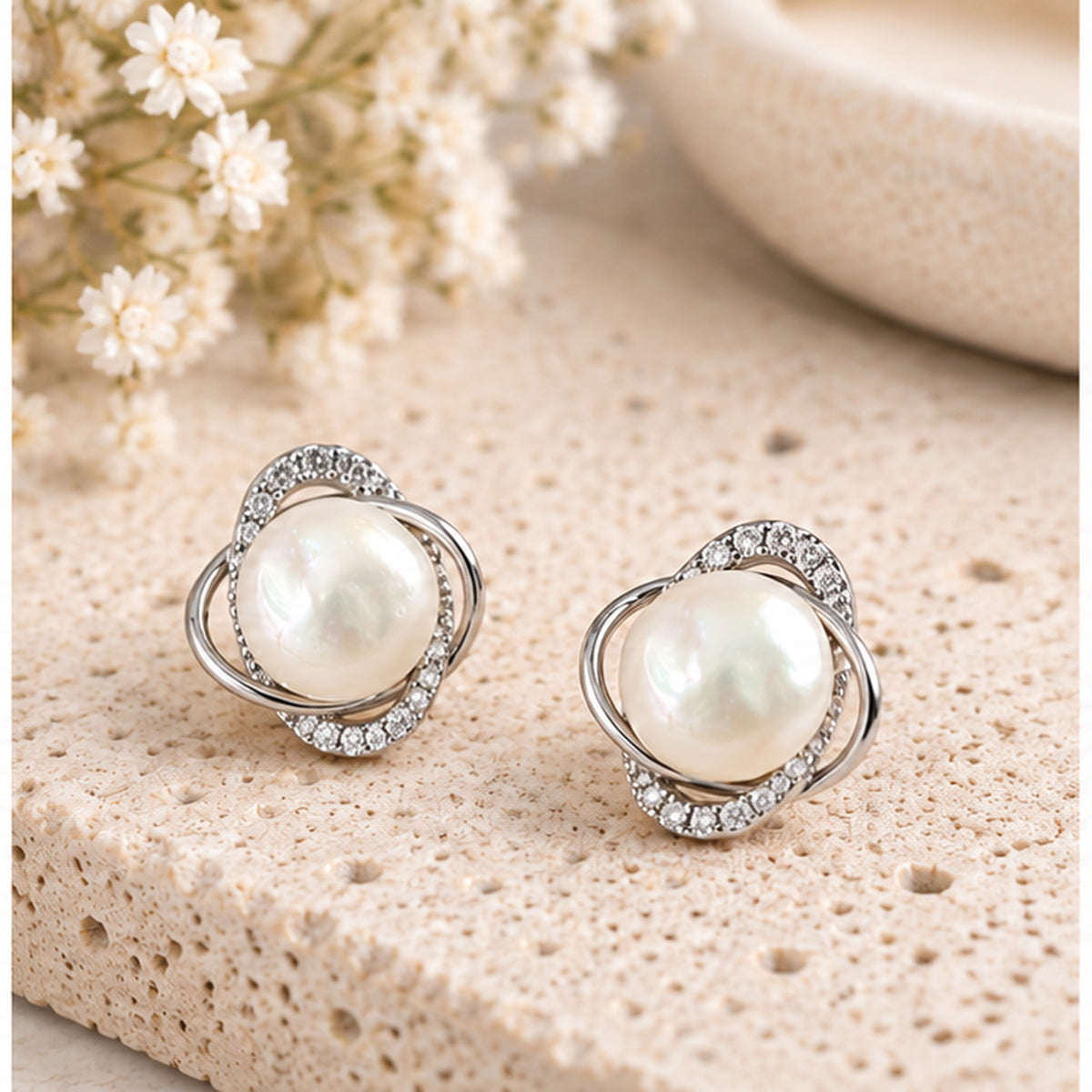 Real pearl orbit stud earrings with intertwined silver loops and clear stone accents in a neutral studio setting