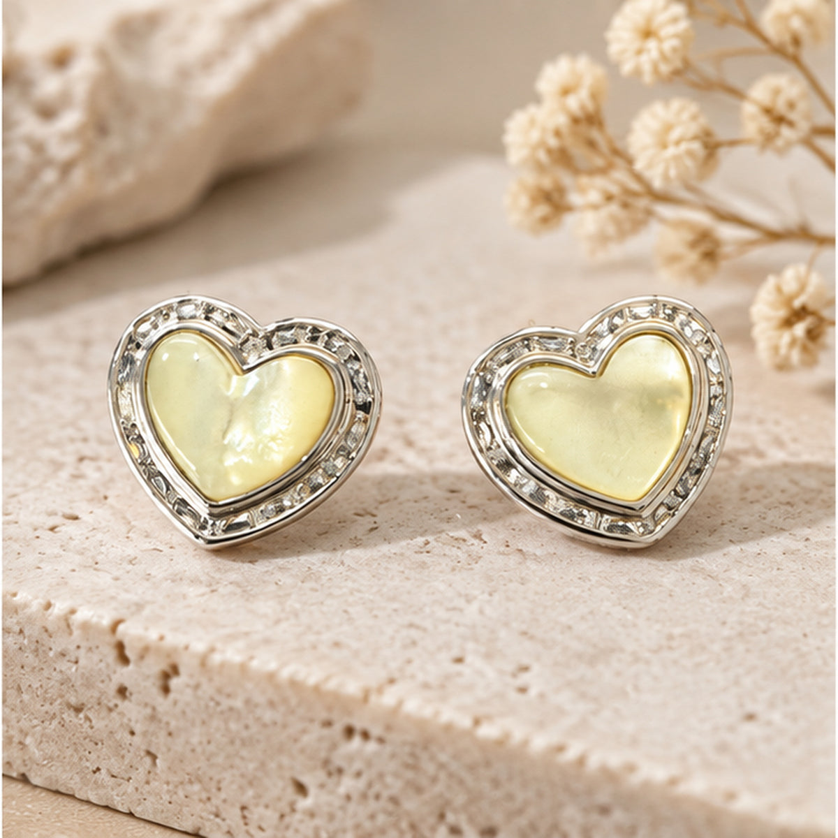 Mother of pearl heart stud earrings with solid sterling silver posts in an elegant neutral studio setting